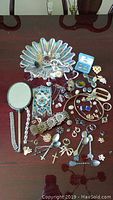 Overview of iridescent glass bowl filled with assorted jewelry items, handheld mirror and mesh purse.