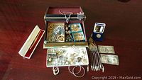 Overview of jewelry box upper and lower trays filled with assorted jewelry, watch box on left, bills and coin on right