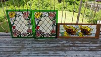 Three decorative stained glass panels on wooden porch railing in natural light.