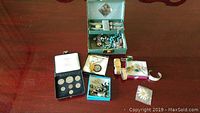 Overview of assorted jewelry, coin collection, watches, and accessories on wooden surface.