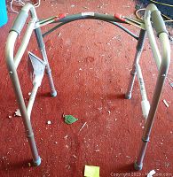 Top view of the silver metallic walker with rubber tips on legs, resting on a red carpet with some small debris around.