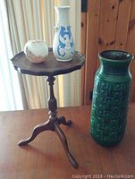 Full view of wood tripod plant stand with three decorative vases on top and the tall green vase next to it.
