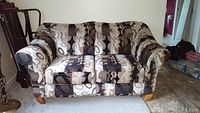 Front view of loveseat showing modern geometric patterned fabric upholstery in neutral colors with padded back and seat cushions and light wooden legs.