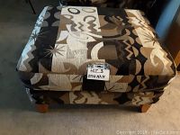 Front view of the ottoman showing geometric pattern fabric and wooden legs