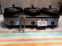 Front view of the Faberware 3-crock slow cooker with all lids on and the lid holder in front.