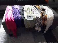 View of eight scarves in various styles and colours laid out on a bench showing full assortment
