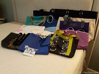 11 assorted tote bags of various colors, sizes and materials displayed on a bed