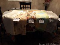 Four tablecloths and one runner laid out on a table showing various colors and patterns with attached size tags.