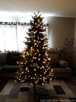 Front view of 6.5 foot artificial Christmas tree lit up with white lights, standing in living room area.