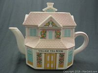 Front view of teapot shaped like a village building with floral decoration and VILLAGE TEA ROOM text.