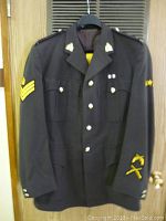 Front view of RCMP tunic showing silver buttons, rank patches on sleeves, embroidered insignia on collar and cuffs, and shoulder epaulets with lettering.