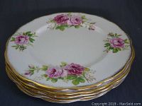 Five stacked vintage Royal Albert American Beauty plates showing floral pink rose motifs with green leaves on white background and gold trim edging.
