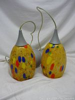 Pair of colorful glass table lamps with light grey conical tops side by side on white background.