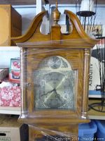 Front view of clock face and upper wooden case with curved top and finial