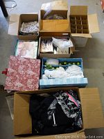 Overview of multiple cardboard boxes containing various home and holiday items including Christmas decorations, punch set, fabric pieces, and clothing