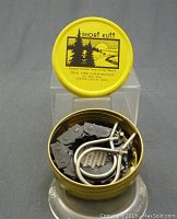 Open yellow metal tin containing the folded Short Kutt chain saw with metal handles inside, showing chain links and handles.