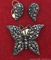 Photo of the butterfly brooch along with the tear drop earrings set, showing the size and overall design against a red background.