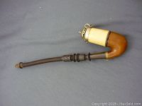 Full side view of the antique meerschaum pipe showing the curved wooden bowl, long dark stem, and metal chamber with ring attachments.