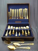 Overall view of wooden case open with blue velvet interior showing top row of knives and bottom compartments of forks and spoons