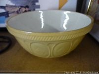Side view showing yellow exterior, rope-like rim detail, and embossed circular designs on ceramic bowl.