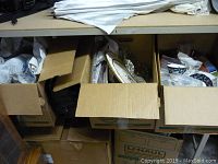 Three open cardboard boxes on a shelf showing packed vintage housewares and decorative items.