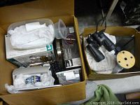 Two boxes filled with various housewares including binoculars, kitchenware, and household items.