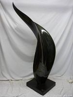 Full view of tall black modern abstract statue with flowing curved design.
