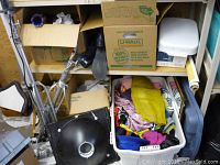 Wide view showing shelves with cardboard boxes, camera tripod and white plastic tote filled with miscellaneous household items.