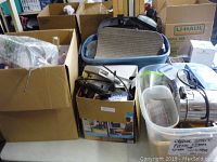Photo showing several cardboard boxes and plastic bins filled with various household and decorative items on a table.