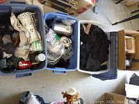 Wide shot showing three blue tubs containing mix of household and decorative items including clothes, metal kitchenware, and glass objects.