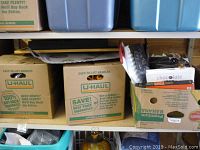 Shelf with U-Haul and Banana boxes containing various household items including decorative objects and books.
