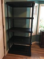 Front angle view of the black plastic storage shelving unit against a wall showing a total of five shelves.