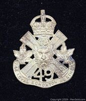 Front view of the vintage Canadian military cap badge showing crown, crossed rifles, lion's head, maple leaves, number 49 and banner text.