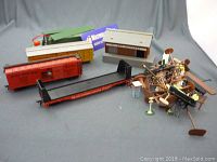 Model train cars, a building, and a collection of scattered train parts and accessories on a gray backdrop.