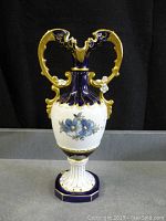 Front view of vintage Royal Dux urn showing height, shape, cobalt blue and white porcelain with blue floral design and gilded handles.