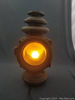 Front lit view of the antique lantern showing warm yellow light from electric bulb inside glass lens.