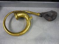 Full view of the circular brass horn with coiled tube and attached rubber bulb.