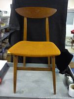 Front view of the vintage mid-mod chair showing the yellow-orange upholstered seat with damage on the left corner.
