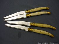 Set of four Languiole steak knives laid out on black surface, showing full length of blades and handles.