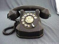 Front view of vintage BC Telephone Co. rotary telephone showing entire phone with handset and coiled cord on blue surface.