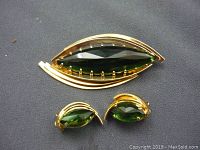 Front of vintage brooch and matching earrings on dark fabric background showing gold tone metal and faceted green stones.