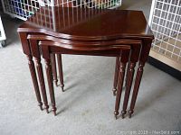 Set of three wooden nesting tables stacked together showing the dark brown polished wood and tapered turned legs