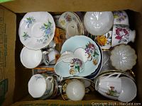Top view of the lot showing multiple porcelain bone china teacups and saucers with floral patterns and gold trim inside a cardboard box.