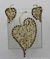 Full set of vintage DODD'S rhinestone leaf jewelry including brooch and earrings displayed on clear stand.