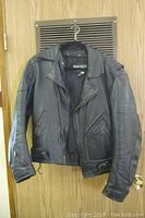 Full view of black leather motorcycle jacket hanging on a door, showing front and sleeves with zipper details.