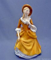 Front view of the Royal Doulton lady figurine in a yellow dress with polka dot trim and wide-brim hat.