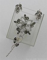 Full view of vintage CONTINENTAL smokey crystal rhinestone flower stem brooch and matching earrings set displayed on a clear stand.