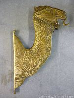 Full view of the wall-mounted brass camel hook showing its textured body and hook.