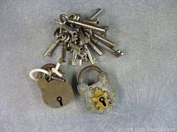 Top view showing two vintage metal padlocks with attached ring of keys all placed on a neutral background.