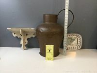 Large copper vessel with handle, paint chipped wooden wall shelf, and ceramic wall mirror all shown together with measuring ruler.